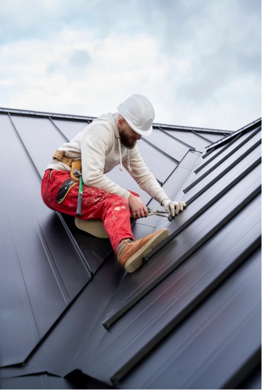 Trabalhador com EPI e cinto de segurança realizando manutenção em telhado metálico inclinado.