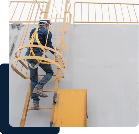 Trabalhador com EPI e cinto de segurança subindo escada marinheiro amarela com gaiola de proteção em área industrial.