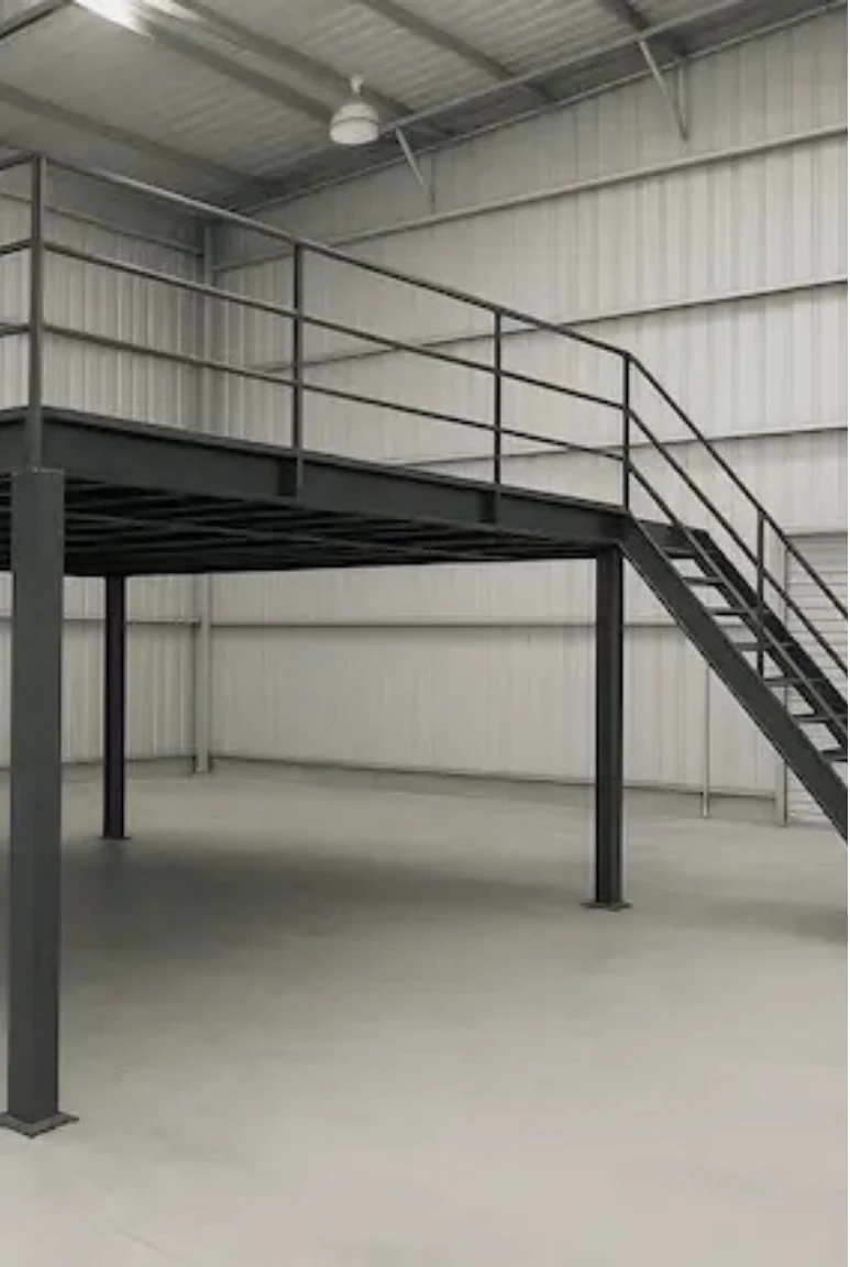 Mezanino industrial modular em aço carbono com escada lateral e guarda-corpo metálico em galpão vazio.